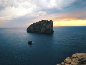 Rock formation in sea against sky during sunset