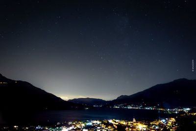 Illuminated city by silhouette mountains against sky at night