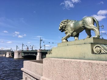 Lion sculpture against sky, water and bridge