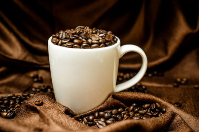 Close-up of roasted coffee beans with cup on fabric