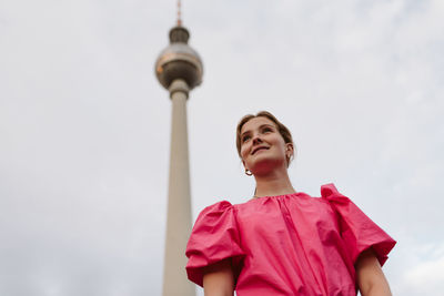 Low angle view of woman looking away against tower and sky