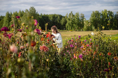 A girl in rubber boots collects autumn flowers on the field