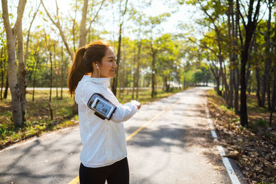 Woman exercising while standing on road against trees