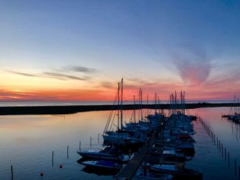 Boats moored in harbor at sunset