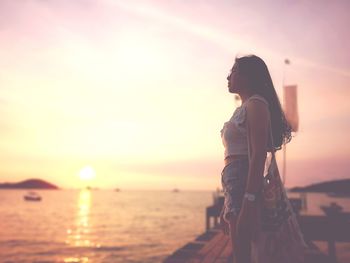 Side view of woman standing on pier over lake against sky during sunset