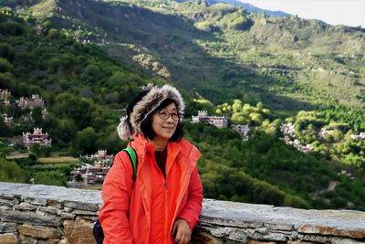 Smiling woman looking away while standing against mountain