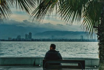 Rear view of man sitting by sea against sky