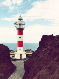 Lighthouse on beach by sea against sky