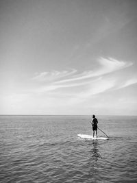 Rear view of man paddleboarding in sea against sky