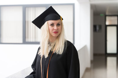 Portrait of young woman wearing graduation gown standing against building