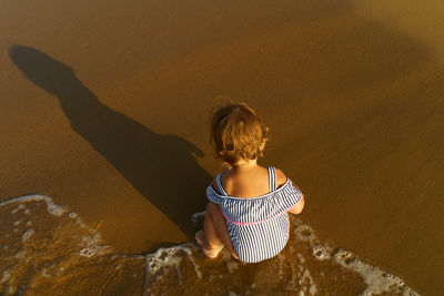 High angle view of cute girl crouching on sand at beach