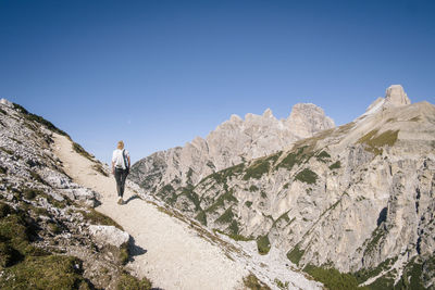 Rear view of man walking on mountain against clear blue sky