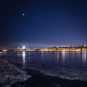 Illuminated city by sea against sky at night