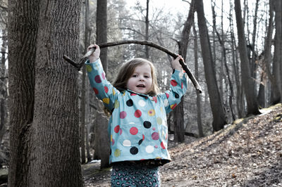 Portrait of cute girl holding stick aloft in forest