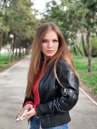 Portrait of young woman standing on road in park