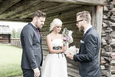 Friend gifting bouquet to bride and groom by wall