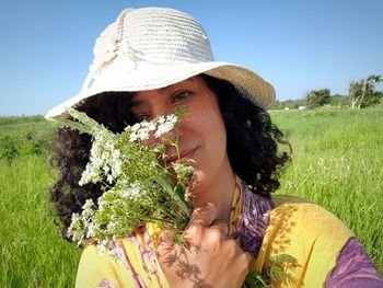 Portrait of woman wearing hat while holding flowers on field against sky