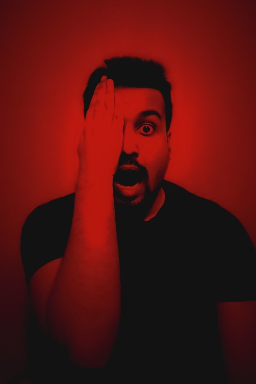 red, one person, portrait, studio shot, adult, indoors, darkness, looking at camera, young adult, human face, headshot, hand, waist up, person, colored background, front view, red background, emotion, men, fear