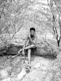 Portrait of boy sitting on fallen tree trunk in forest