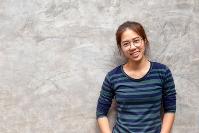 Portrait of smiling young woman standing against wall