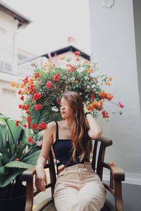 Thoughtful young woman looking away while sitting on chair by potted plants
