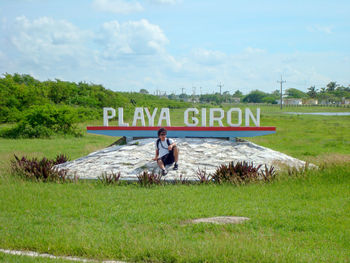 Man sitting on field against sky