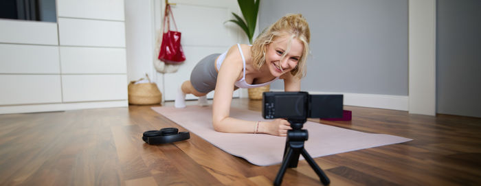 Portrait of young woman using mobile phone while sitting on hardwood floor