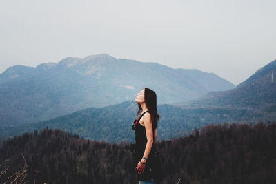 Side view of woman standing on mountain against sky