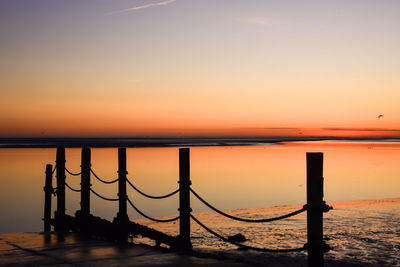 Silhouette wooden posts on beach against sky during sunset