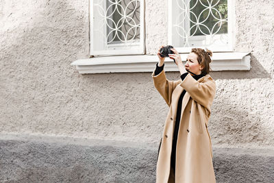 Woman standing by window on wall of building and shooting something 