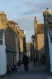 Rear view of man walking on alley amidst buildings in city