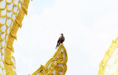 Low angleview of bird perching on sculpture against sky