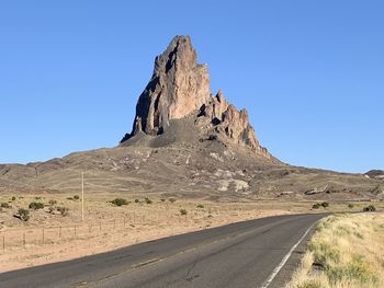 Scenic view of desert road against clear blue sky