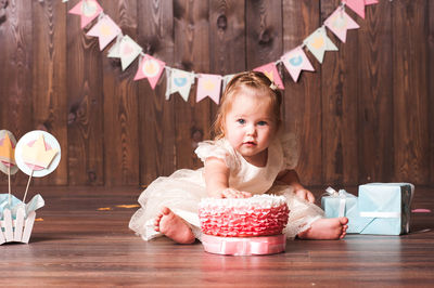 Cute baby girl with cake sitting on floor