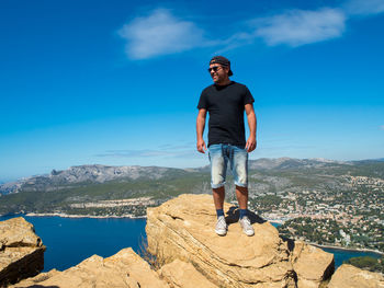 Full length of young man standing on mountain against blue sky