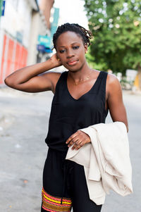 Young woman standing outside, her jacket hanging on her left arm and her right hand