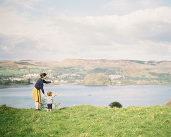 Mother with son standing on land against lake