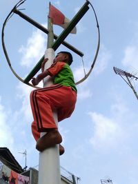 Low angle view of boy climbing on pole against sky