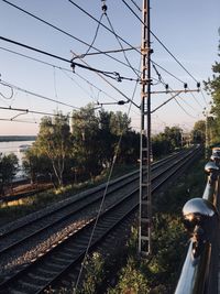 Electricity pylon by railroad tracks against sky