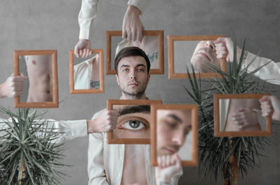 Digital composite image of hands holding picture frames around man standing against wall