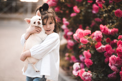 Smiling kid girl 3-4 year old holding pet dog over flower background closeup. looking at camera.