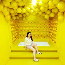 Full length portrait of woman sitting at bathtub against yellow wall