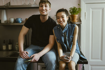 Portrait of smiling young friends sitting together on kitchen counter at home