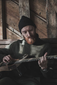 Young man playing guitar while sitting against wall