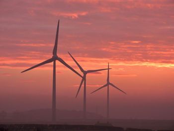 Silhouette windmill on landscape against dramatic sky during sunset