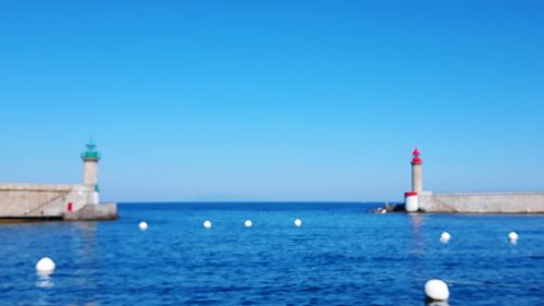 Lighthouse by sea against clear blue sky