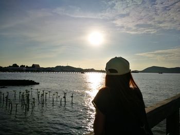 Rear view of woman standing by sea against sky during sunset