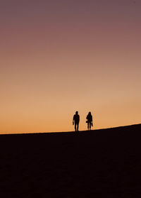 Silhouette people standing on land against sky during sunset