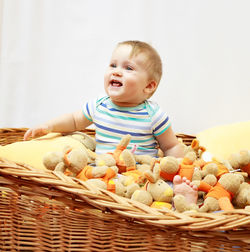 Cheerful baby boy sitting with toys in wicker basket