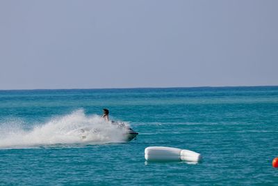 Young woman riding motorboat on sea against clear blue sky during sunny day